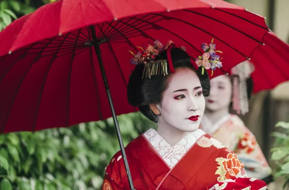 Beautiful Maiko with red clothing and umbrella in the streets of Kyoto, Japan