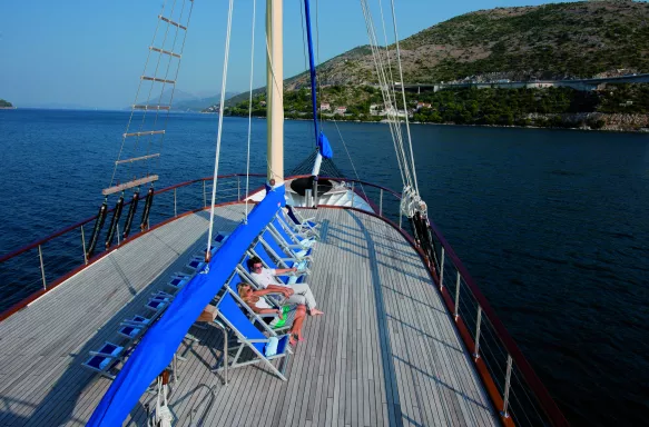 Exterior shot of the bow of a yacht with people sunbathing on deck chairs