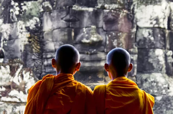 The back of two Buddhist monks at Bayon Temple looking at stone Buddah head in Cambodia