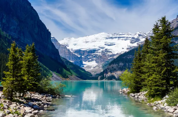 Beautiful Lake Louise with Victoria Glacier in the background and a glistening emerald lake. Several canoes can be seen at a distance on the lake.