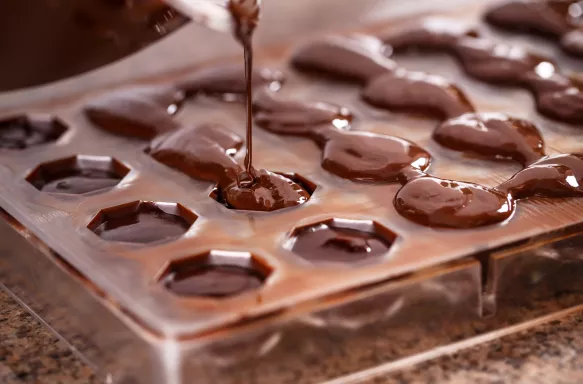 Close-up of chocolate being poured into a plastic mold to make praline