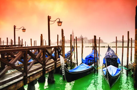 Venice canal boats lined up besides a dock under a warm sunset sky