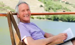 Smiling man relaxing in a chair while reading, on a boat deck