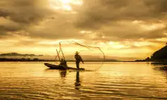 A fisherman in a boat throwing a net on the lake during sunset