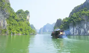 A river boat moving across the turquoise waters of Halong Bay 