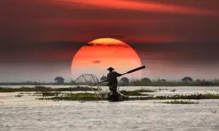 Vietnamese fisherman on his boat during sunset, balancing a oar paddle