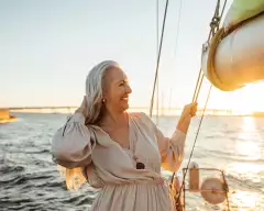 Senior woman adjusting her hair and enjoying sunset on private yacht