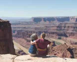An mature couple sitting atop a canyon cliff edge, overlooking the valley below in Utah