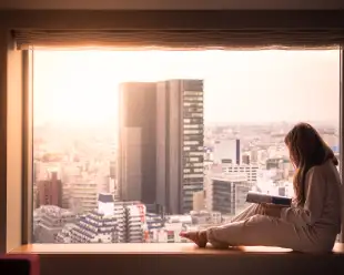 A woman in her pyjamas, looking out of her hotel window at the cityscape of Shibuya, Tokyo. 