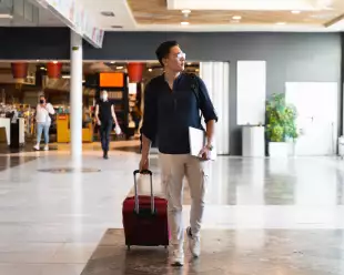 Man walking through an airport with his laptop and suitcase