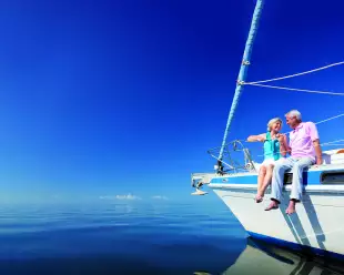 Happy senior couple sitting on the bow of a sail boat on a calm blue sea