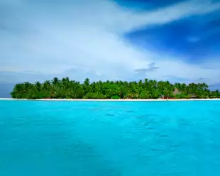 Stunningly turquoise and clear ocean waters surrounding Alimathà island with lush vegetation in the Maldives
