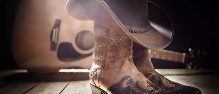 Cowboy boots with cowboy hat on top, a guitar in the background