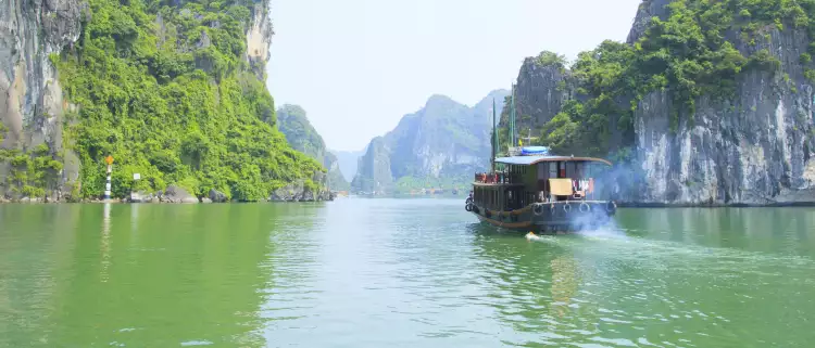 A river boat moving across the turquoise waters of Halong Bay 