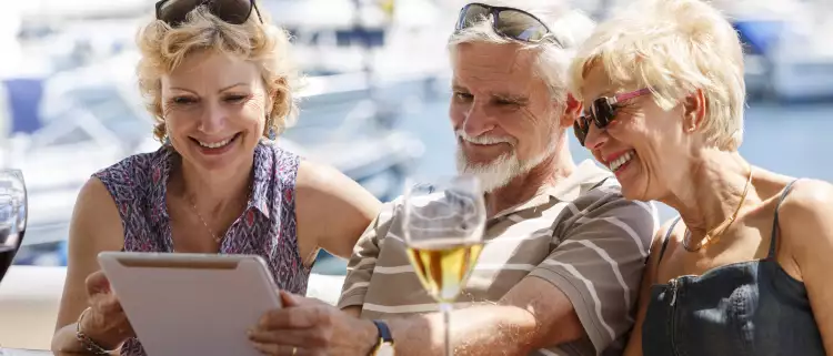 Senior friends smiling and using a digital tablet on a yacht.