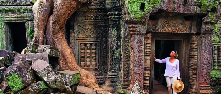 A Woman paused in the doorway of an ancient ruin of Ta Prohm, looking in up in admiration.