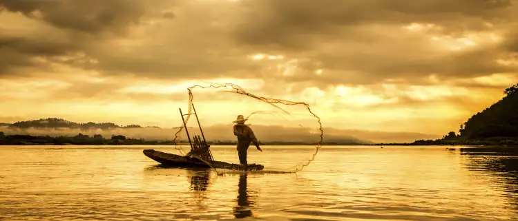 A fisherman in a boat throwing a net on the lake during sunset