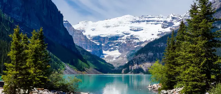 Beautiful Lake Louise with Victoria Glacier in the background and a glistening emerald lake. Several canoes can be seen at a distance on the lake.