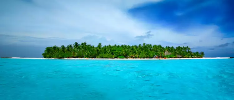 Stunningly turquoise and clear ocean waters surrounding Alimathà island with lush vegetation in the Maldives