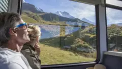 Mature couple in moving train enjoying the passing view of the Swiss alps and alpine area.