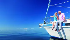 Happy senior couple sitting on the bow of a sail boat on a calm blue sea