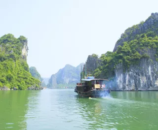 A river boat moving across the turquoise waters of Halong Bay 