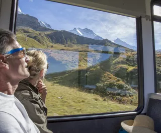 Mature couple in moving train enjoying the passing view of the Swiss alps and alpine area.