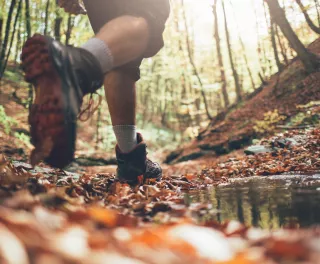 Close-up of hiker boots crossing mountain forest stream in autumn