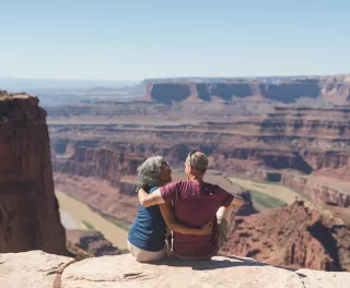 An mature couple sitting atop a canyon cliff edge, overlooking the valley below in Utah