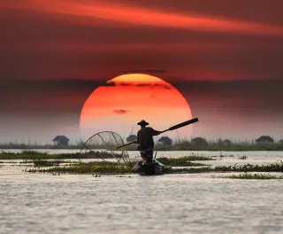 Vietnamese fisherman on his boat during sunset, balancing a oar paddle