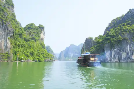 A river boat moving across the turquoise waters of Halong Bay 