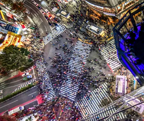 Aerial view of busy Shibuya crossing in Tokyo in-between large skyscrapers adorned with advertising screens, Japan