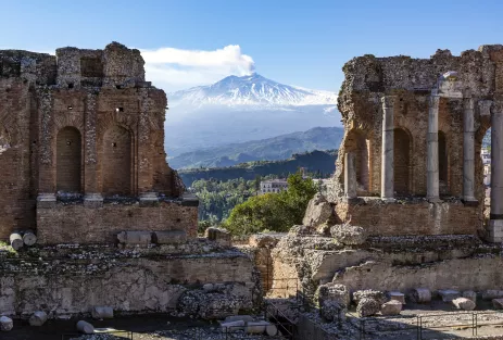 Distant view of Volcano Etna in Sicily seen through ruins of ancient amphitheater in Taormina