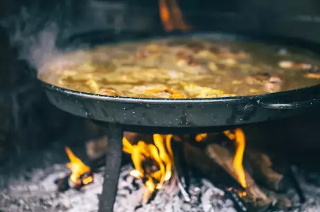 Velencian Paella being cooked over an open fire in a metal pan.